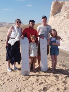 a group of people standing in the sand with a snowboard at Abo Yusre Sfari in Bawiti