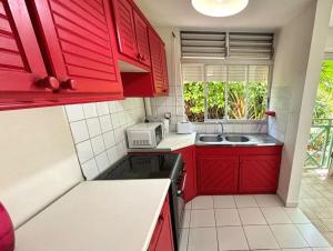 een kleine keuken met rode kasten en een spoelbak bij Le refuge de Chrystel : Plage accessible à pied in Le Gosier