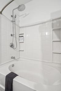 La salle de bains blanche est pourvue d'une baignoire et d'une douche. dans l'établissement CozySuites Mill District pool gym # 06, à Minneapolis
