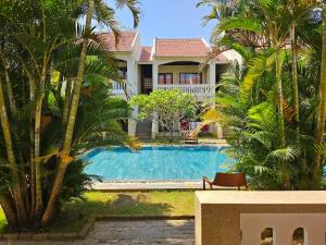 a swimming pool in front of a house with palm trees at Hoian Village Lodge in Hoi An