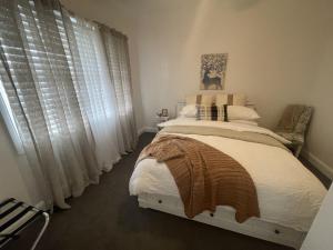 a bedroom with a bed with white sheets and windows at Hamptons House on Hunter with fire pit in Aberdare