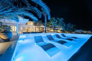 Sanarte Villas Mykonos في مدينة ميكونوس: حمام سباحة في الليل مع أضواء زرقاء