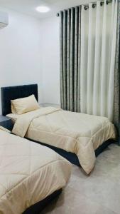 a bedroom with two beds and a window with curtains at شقة فندقية فاخرة - غرفتا نوم - تلاع العلي in Umm Uthainah