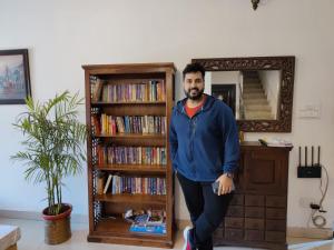 a man standing next to a book shelf with dvds at Himtrek Stays Delhi in New Delhi