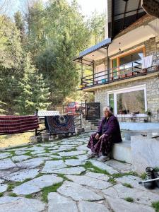 a woman sitting on a bench in front of a house at Rishi Villa in Manāli