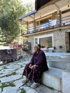 an older woman sitting on a ledge in front of a house at Rishi Villa in Manāli