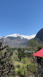 a view of a snowy mountain range with a red roof at Rishi Villa in Manāli