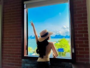 Una mujer con un sombrero mirando por una ventana en Cánh Buồm Homestay - Tuần Châu, en Ha Long