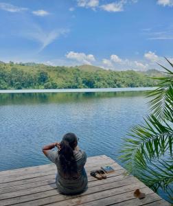 Una donna seduta su un molo che guarda un lago di Baranko Villa a Fort Portal