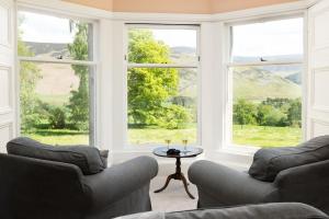 a living room with two couches and a table and windows at Mossfennan House & Annexe in Drummelzier