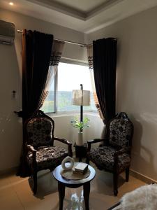 uma sala de estar com duas cadeiras, uma mesa e uma janela em Modern 2 Bedroom Apartment with GYM&POOL em Lahore