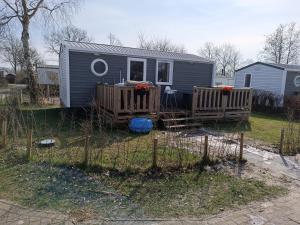 een klein huisje in een tuin met een hek bij BJ Chalets - Robbengat 85 - Gezellige, kindvriendelijke chalet op vakantiepark Lauwersoog! Vroege incheck! in Lauwersoog