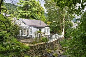 a white house with a stone wall and trees at Finest Retreats - Nant Cottage in Llangelynin