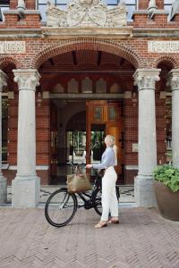 kobieta stojąca obok roweru przed budynkiem w obiekcie Hotel Botanique Breda w mieście Breda