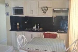 cocina con armarios blancos, mesa y fregadero en Appartamento Aruba Juan Dolio fronte mare, en Juan Dolio