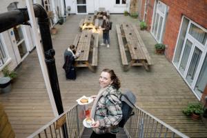 une femme debout sur un balcon tenant une assiette de nourriture dans l'établissement Wombat's City Hostel London, à Londres