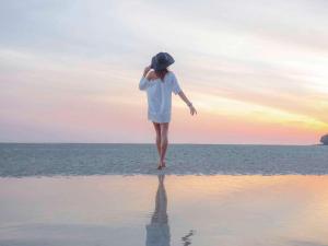Pullman Phuket Panwa Beach Resort في شاطئ بنوا: امرأة تمشي على الشاطئ عند غروب الشمس