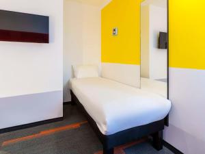 Cama pequeña en habitación con paredes blancas y amarillas en greet Hotel Nancy Sud, en Houdemont