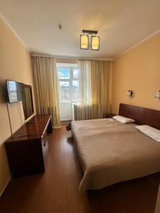 a bedroom with a bed and a desk and a window at Hotel Alma-Ata in Borovoye