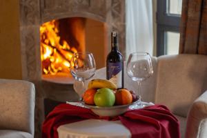 a bowl of fruit and wine glasses on a table with a fireplace at Milagro of Cappadocia in Uchisar