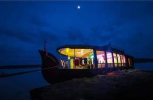 a boat with lights on the water at night at Sukūn Houseboats in Kannur