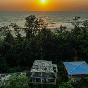 zachód słońca nad plażą z domem i oceanem w obiekcie Dakshinamurthi Beach Stay w mieście Gokarna
