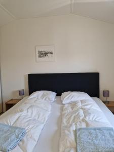 een bed met witte lakens en een zwart hoofdeinde bij Chalet in Lauwersoog