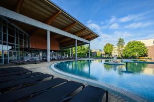 a swimming pool with lounge chairs in front of a building at Hotel Azur Siofok in Siófok
