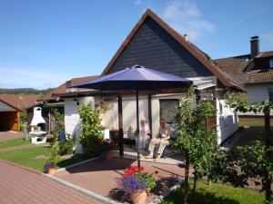 two people sitting under an umbrella outside a house at Ferienhaus-Pahl-in-Wolfshagen in Wolfshagen
