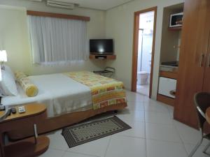 a bedroom with a bed and a desk and a television at Gloria Garden Suites in Macaé