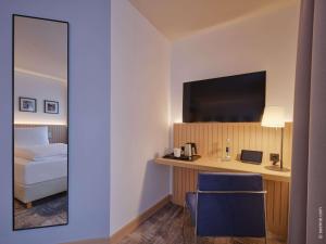 Habitación de hotel con cama y escritorio con TV. en Dorint Hotel Würzburg, en Würzburg