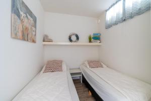 Dos camas en una habitación con paredes blancas y una ventana. en Appartementencomplex Juliana 88, en De Koog