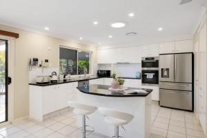 a kitchen with white cabinets and a island with bar stools at Habourlights 5BR River Front Private Pool & Dock in Gold Coast