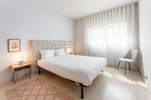 a white bedroom with a large bed and a chair at GuestReady - Modern apt near Matosinhos Beach in Matosinhos