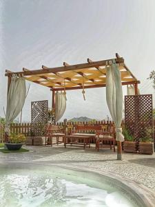 a wooden pergola with benches and a swimming pool at Appartamento•Palermo in Torretta