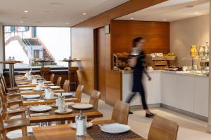 uma mulher a andar por um restaurante com mesas de madeira em Hotel D - Design Hotel em Basileia
