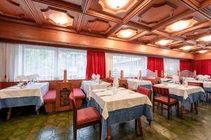 カンピテッロ・ディ・ファッサにあるHotel Grohmannの白いテーブルと椅子、赤いカーテンが備わるレストラン