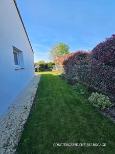 ein Garten neben einem weißen Gebäude und einer Mauer in der Unterkunft Chez Tina jolie maison à 12 min du Puy du Fou in Les Herbiers