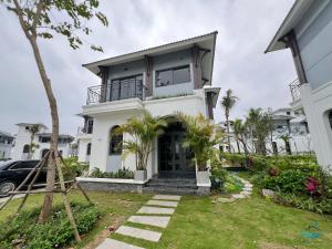 a white house with a balcony and a yard at Rosa Villa - Sonasea Vân Đồn in Cái Rồng