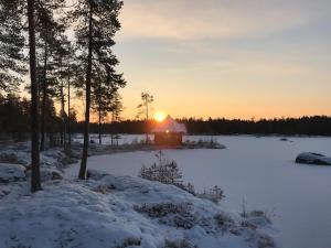 ハラマにあるHUNURIJÄRVI RESORT*****の雪の中のキャビン(夕日を背景に)