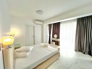 a white bedroom with a bed and a large window at LUXURY RESIDENCE Apartments & Studio in Mamaia