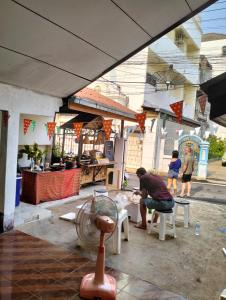 un homme assis sur une table devant un magasin dans l'établissement Peekaboo house, à Ubon Ratchathani