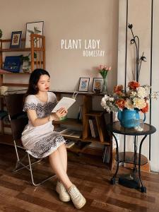 a woman sitting in a chair reading a book at Plant Lady Homestay Cao Bằng in Cao Bằng