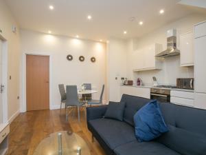 Ealing Queen of the Suburbs One Bedroom Apartment Pass the Keys في لندن: غرفة معيشة مع أريكة زرقاء ومطبخ