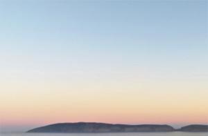 een zonsondergang over de oceaan met bergen op de achtergrond bij Plettenberg View in Plettenbergbaai
