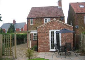a brick house with a patio with an umbrella at Avocet Cottage in Dersingham
