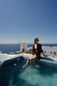 a woman sitting on the edge of a swimming pool at The Sunset Windmill in Oia