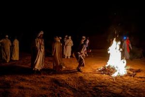 a group of people standing around a bonfire at night at Mhamid Luxury Camp in Mhamid
