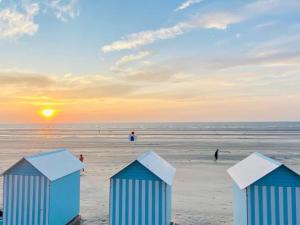 drei blaue und weiße Strandhütten am Strand bei Sonnenuntergang in der Unterkunft Loft à deux pas de la plage in Dunkerque