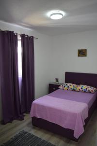 a bedroom with a bed with purple curtains and a window at Milica Apartments in Sutomore